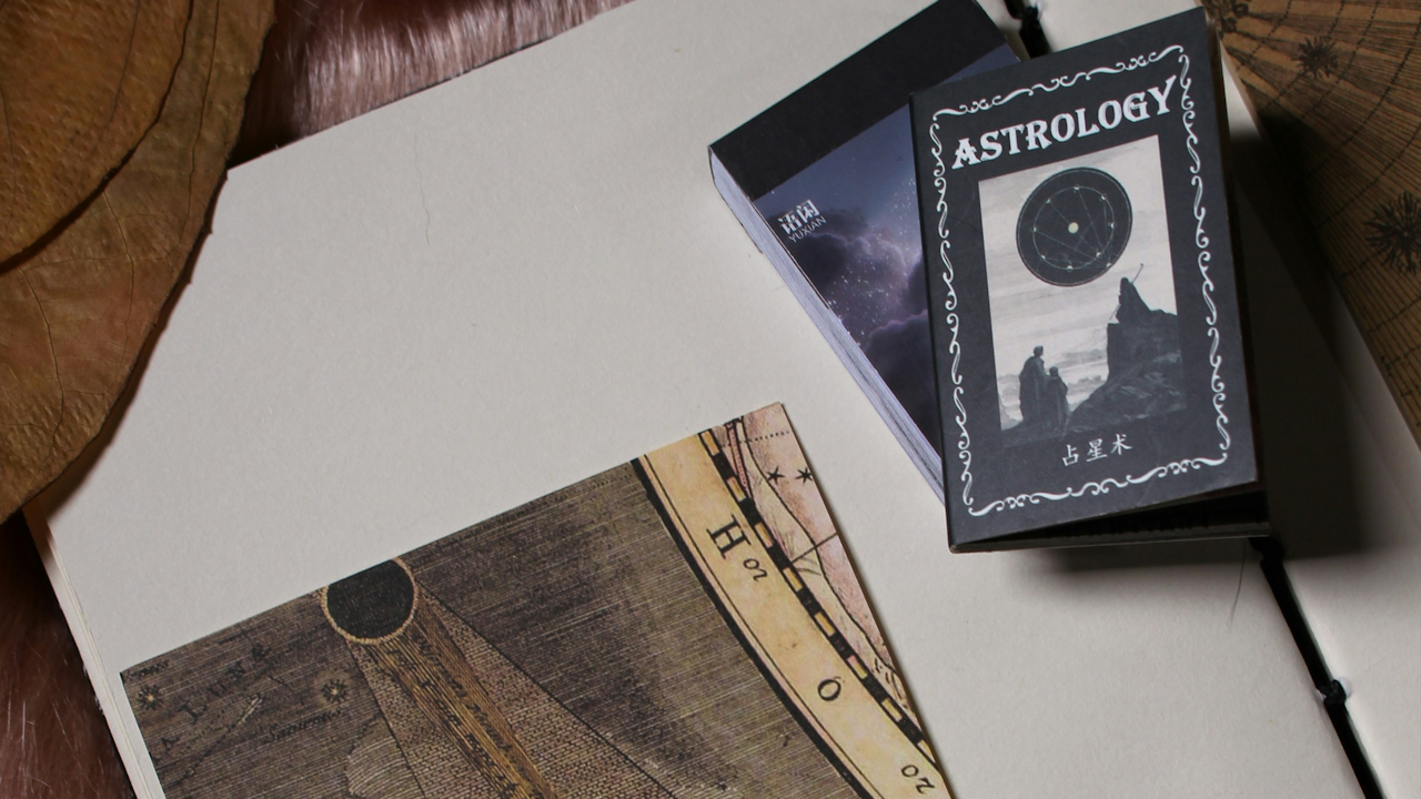 A dark-toned image showing a small book titled Astrology and a vintage-style star chart on a notebook.