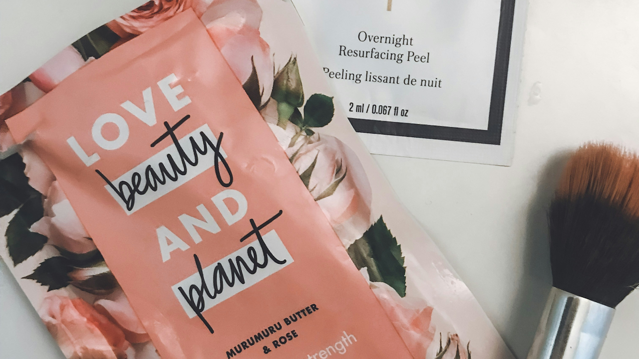 A high-angle close-up shot of a Love Beauty and Planet Murumuru Butter and Rose hair mask next to a makeup brush.