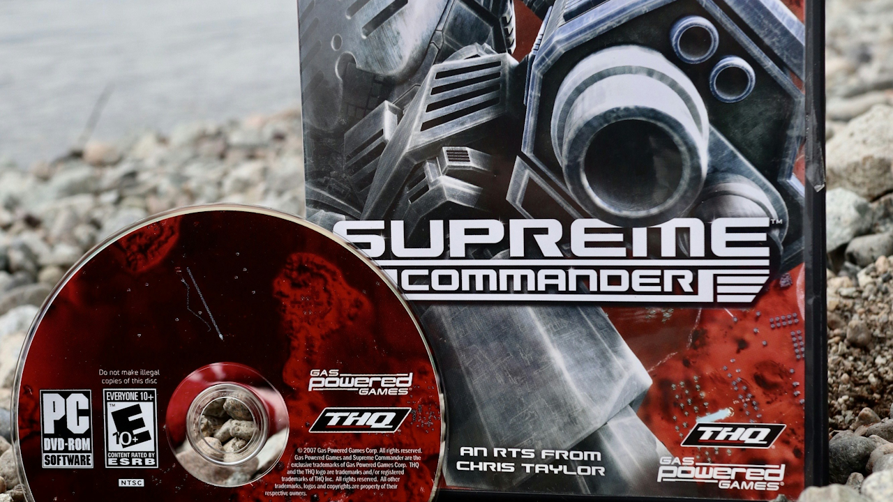 A CD labeled "SUPREINE COMMANDER" along with its box, which features the text "THQ SOFTWARE AN RTS FROM CHRIS TAYLOR Powered -GAMES." The setting appears to be outdoors with a ground surface that includes rocks.