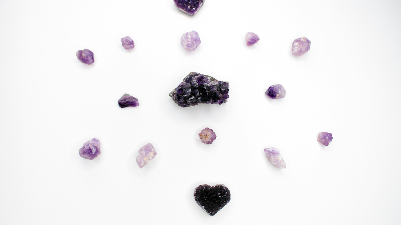Purple amethyst crystals and a black heart-shaped stone arranged on a white background.