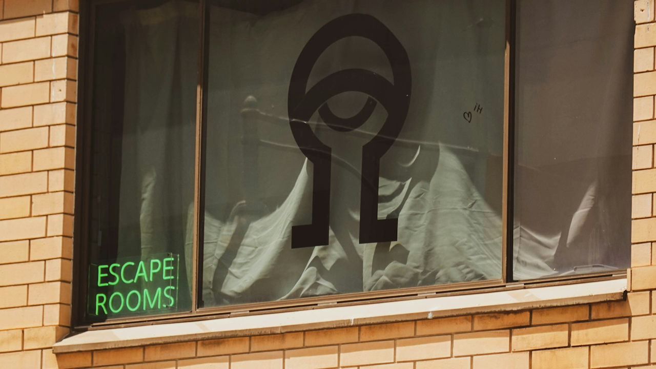 A window featuring a sign that reads "ESCAPE ROOMS," set in an urban outdoor environment.