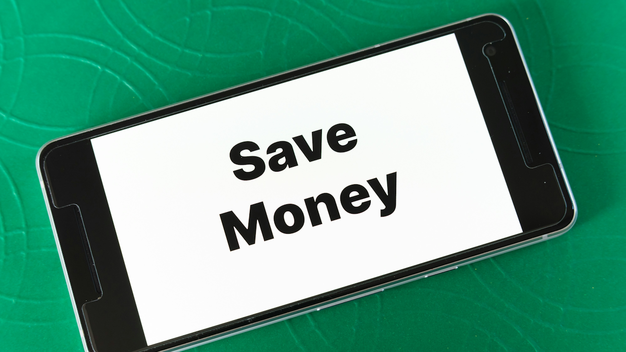 Smartphone on green surface displaying "Save Money" text, suggesting financial savings tips.