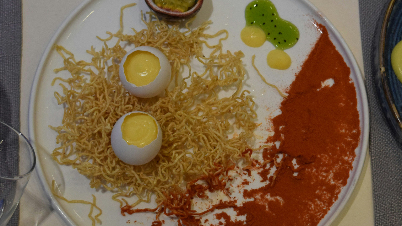 A close-up of a plate of food featuring scrambled eggs mixed with noodles, garnished with herbs, set on a wooden table.