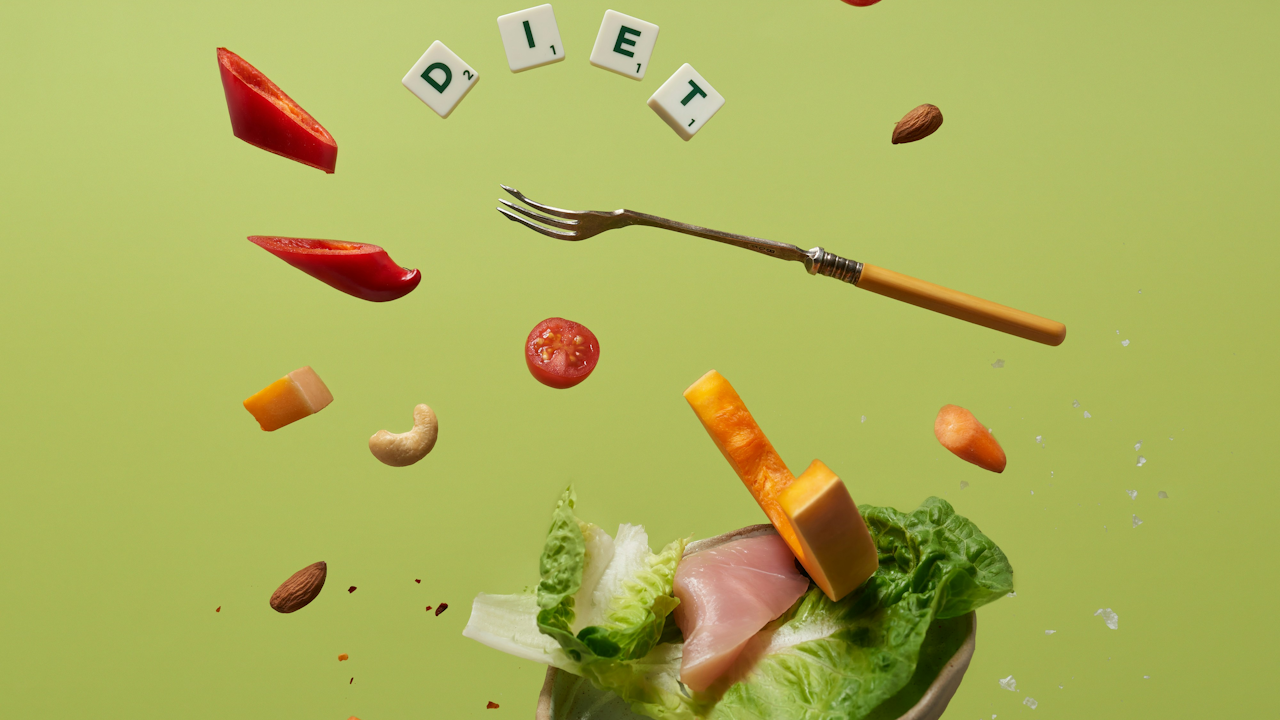 A vibrant salad with floating vegetables, nuts, and a fork, surrounded by "DIET" tiles, set against a green background.