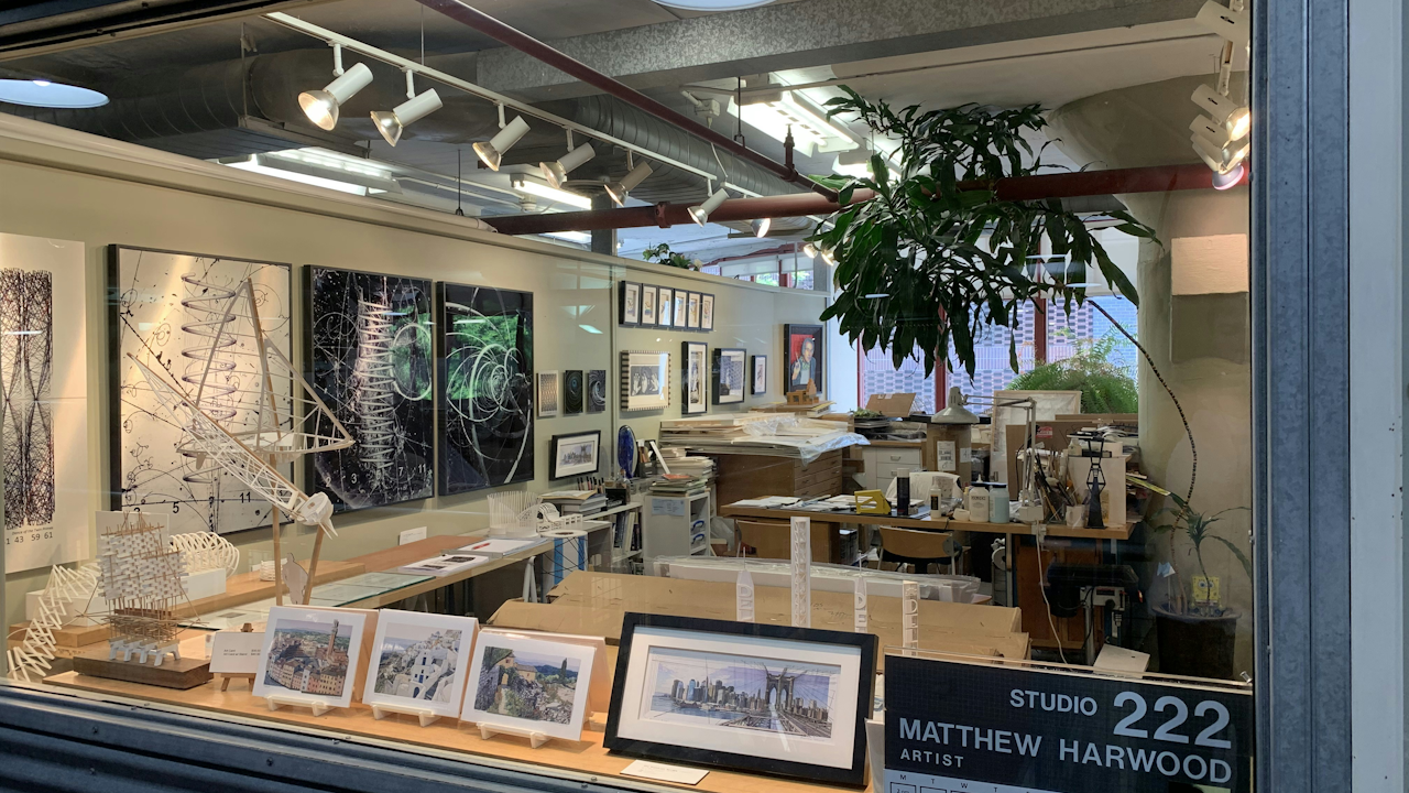 A room featuring various artworks and pictures displayed on the walls, with a window allowing natural light to enter. The space is part of Studio 222 by Matthew Harwood Antist and includes elements like picture frames, an indoor setting, and a ceiling that adds to its ambiance.