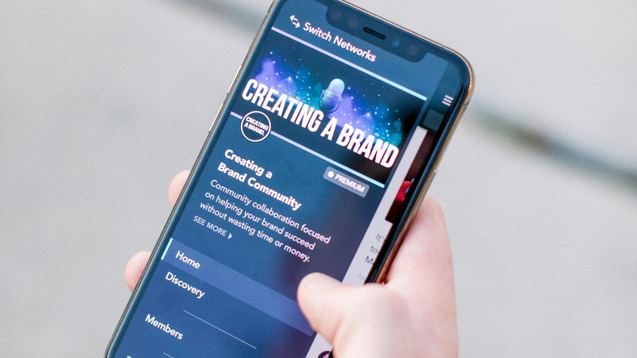 Hand holding smartphone displaying "Creating a Brand" page on Switch Networks app, with Home, Discovery, and Members options.