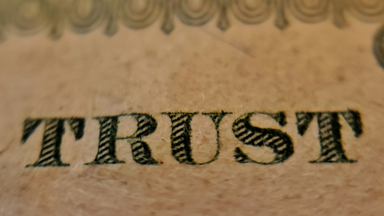 A close-up image of the word "TRUST" written in an elegant, flowing calligraphy style with a focus on the intricate details of the font.