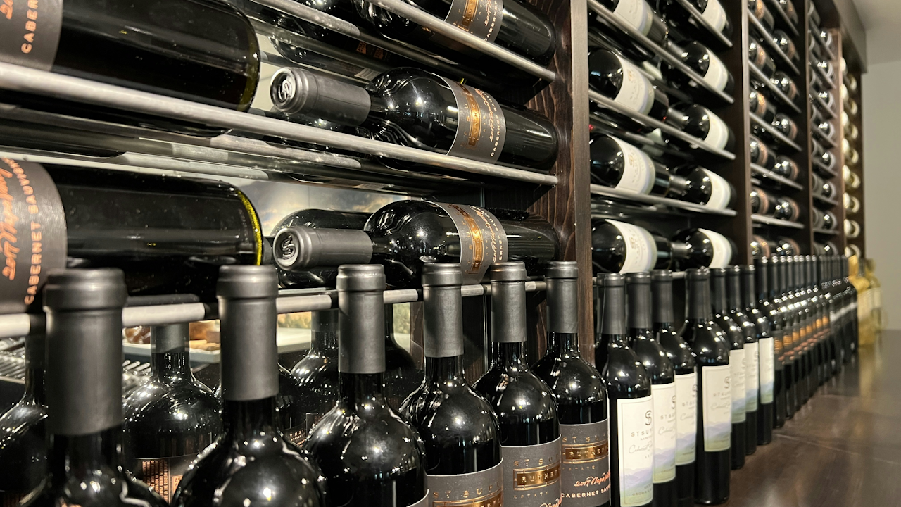 Rows of wine bottles stored in wooden racks, featuring Cabernet Sauvignon labels, in a well-organized cellar.