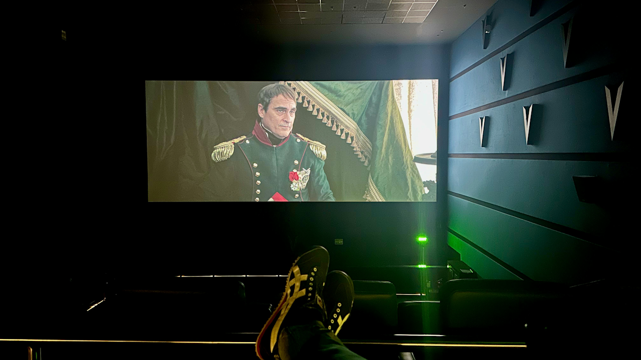 A person lying on a couch, focused on watching a movie. The room is dimly lit, creating a cozy atmosphere.