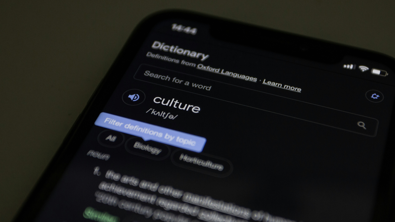 Smartphone displaying Oxford Dictionary app with "culture" definition, phonetic spelling, and topic filters on dark mode.