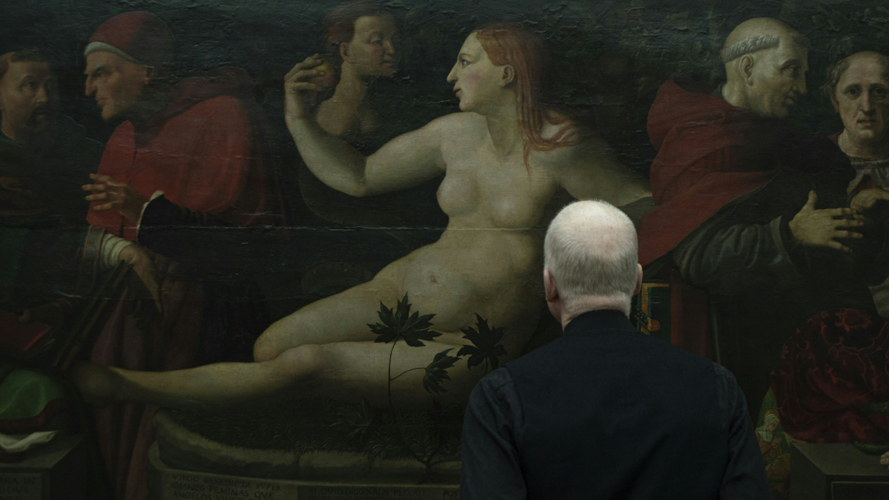 Man observing Renaissance painting of reclining nude figure with figures in red robes, set against dark background with plants.