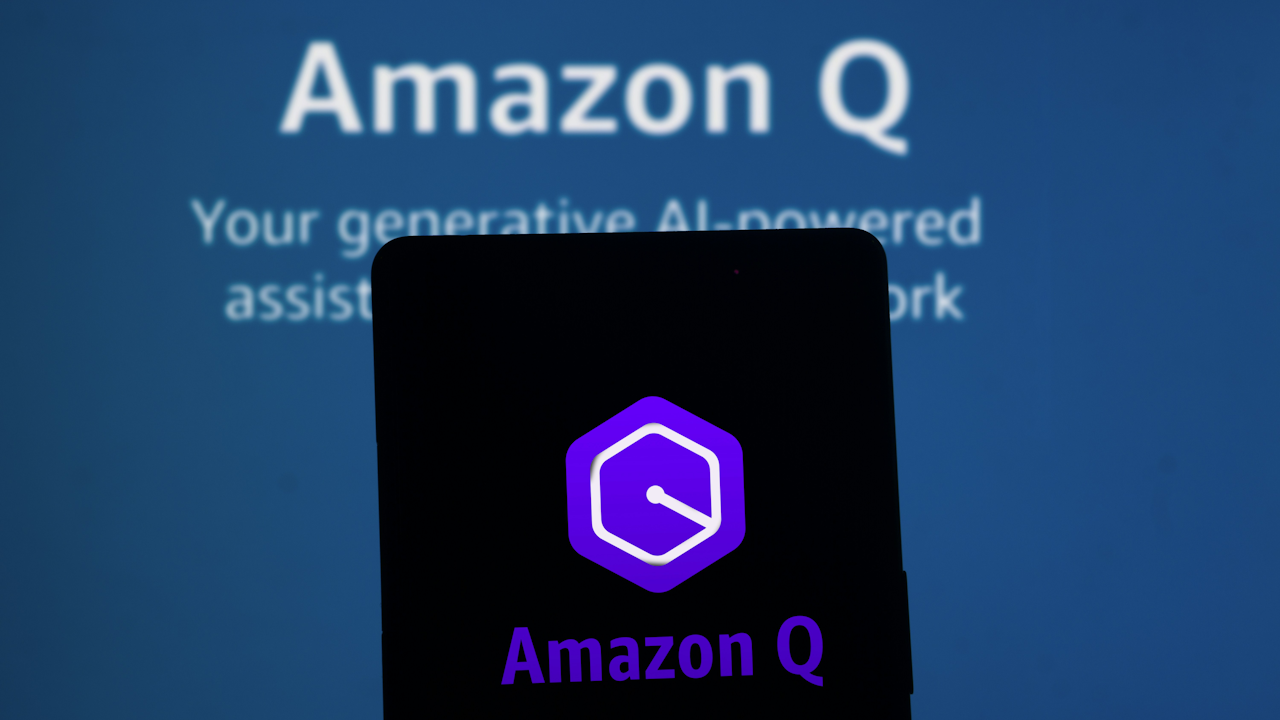 A mobile phone screen displays the Amazon Q logo, a purple hexagonal shape with a stylized 'Q' inside. In the background, a larger screen shows the text 'Amazon Q' and a description of the generative AI assistant.