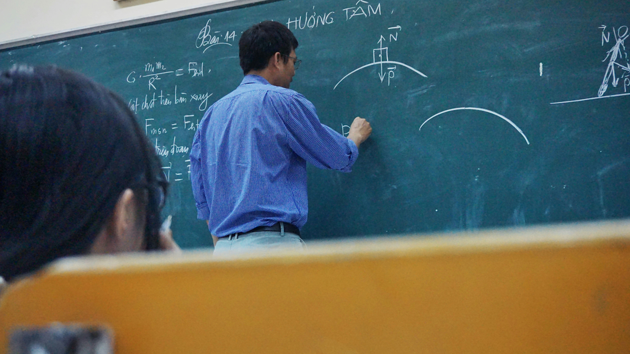 Teacher writing equations on blackboard in classroom, student in foreground, focused on lesson.