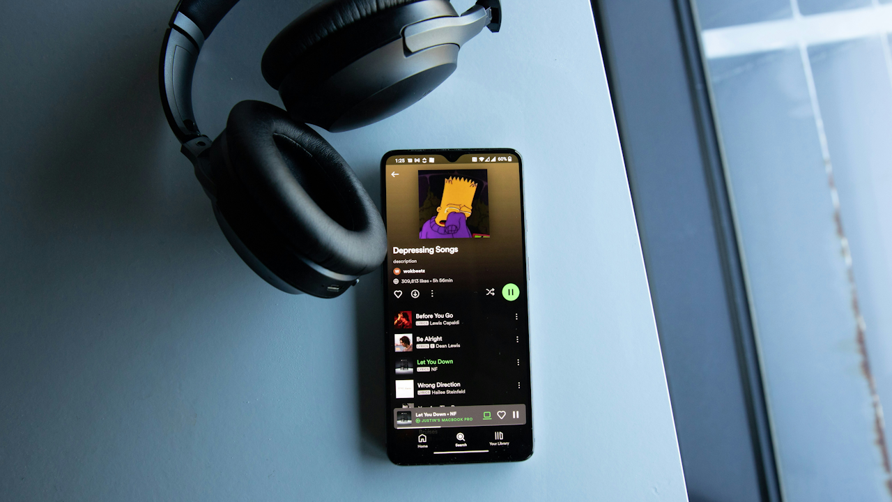 Headphones on a table next to a smartphone displaying a "Depressing Songs" playlist with a Bart Simpson cover.